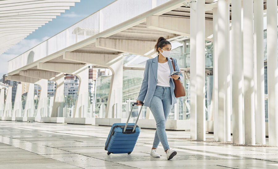 Une femme portant un masque, transportant son bagage à l'aéroport.