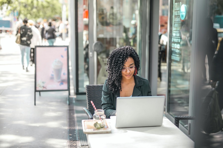 jeune-femme-ethnique-utilisant-un-ordinateur-portable-tout-en-ayant-une-boisson-savoureuse-dans-un-cafe-de-rue-moderne